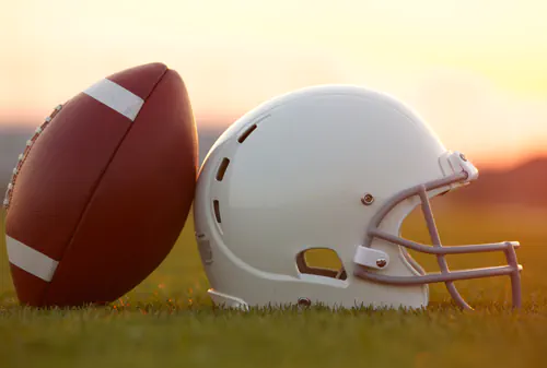 Football and helmet on field at sunset